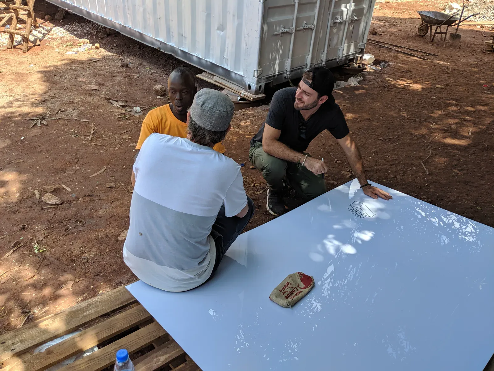 Grant kneeling with community members, painting a mural panel together on the ground
