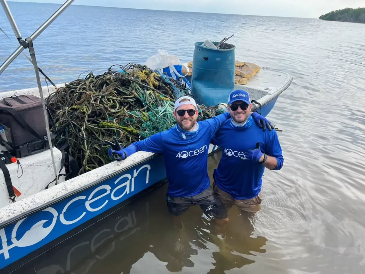 Two 4ocean crew hauling a net-loaded boat through shallow water