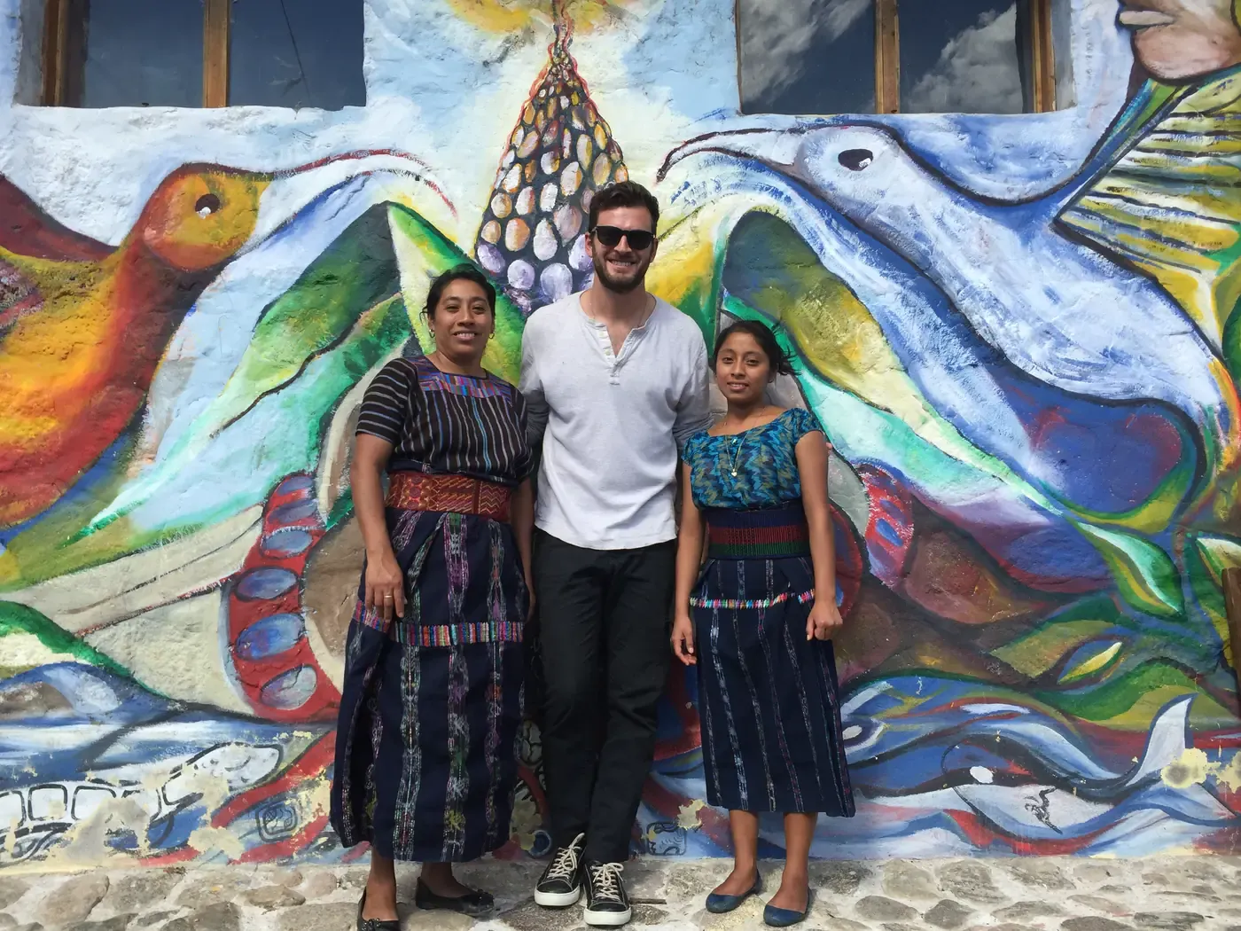 Grant with two Mayan women in traditional dress in front of a painted mural in Guatemala