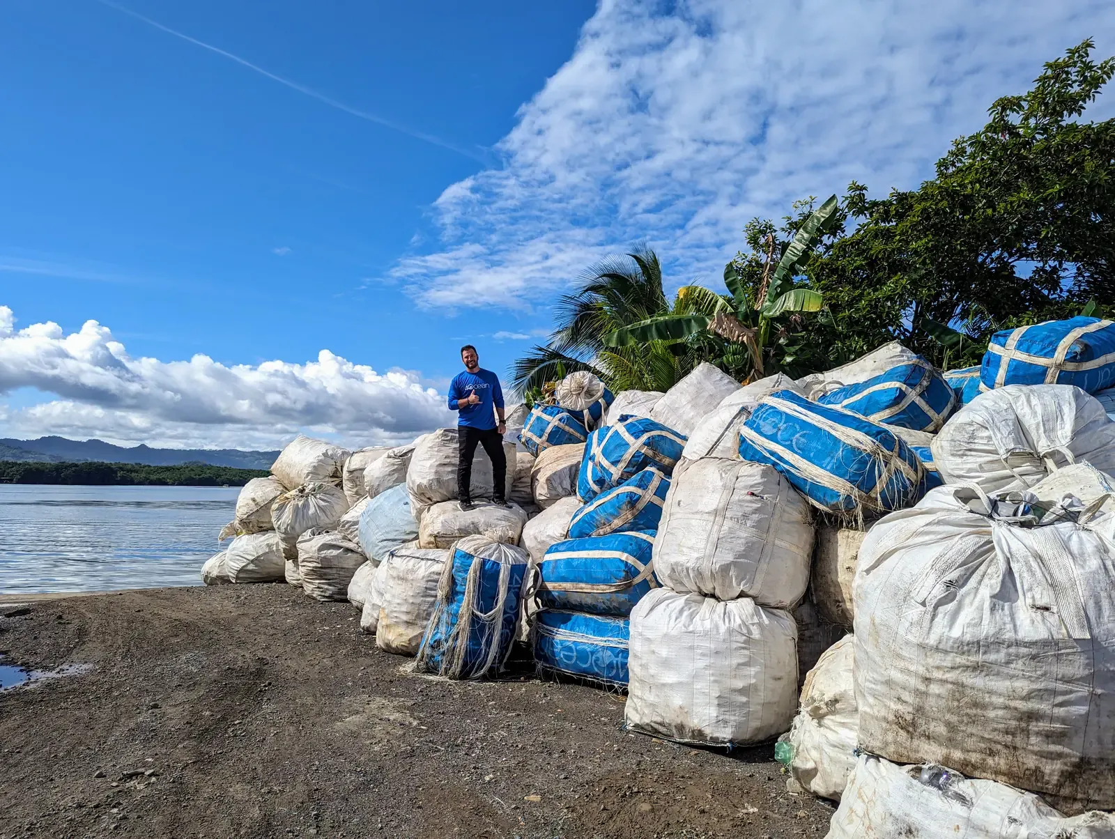 Grant standing on a shoreline stack of bagged plastic recovered from the coast